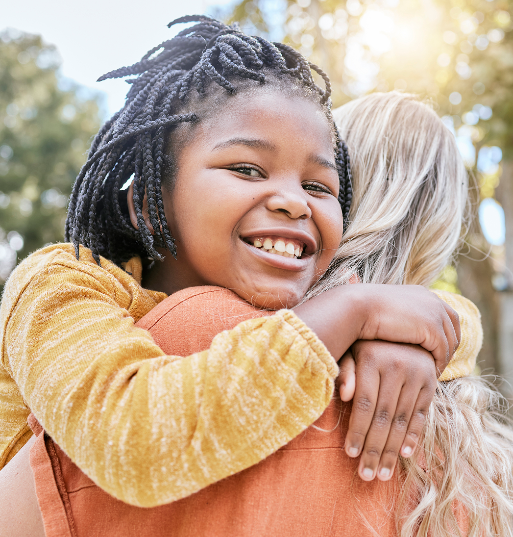 Two children hugging outdoors, smiling in warm sunlight.