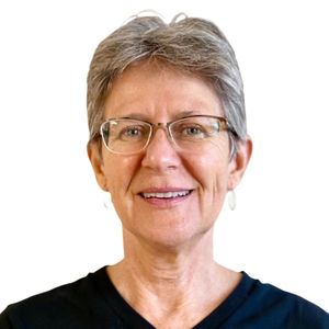 Smiling woman with short gray hair and glasses wearing a black top against a white background
