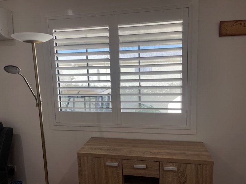 A Living Room With a Lamp and a Window With Shutters — Dennys Upholstery & Outdoor Blinds In Evans Head, NSW