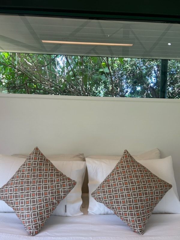 A Bed With Pillows and a Window With Trees in the Background — Dennys Upholstery & Outdoor Blinds In Casino, NSW