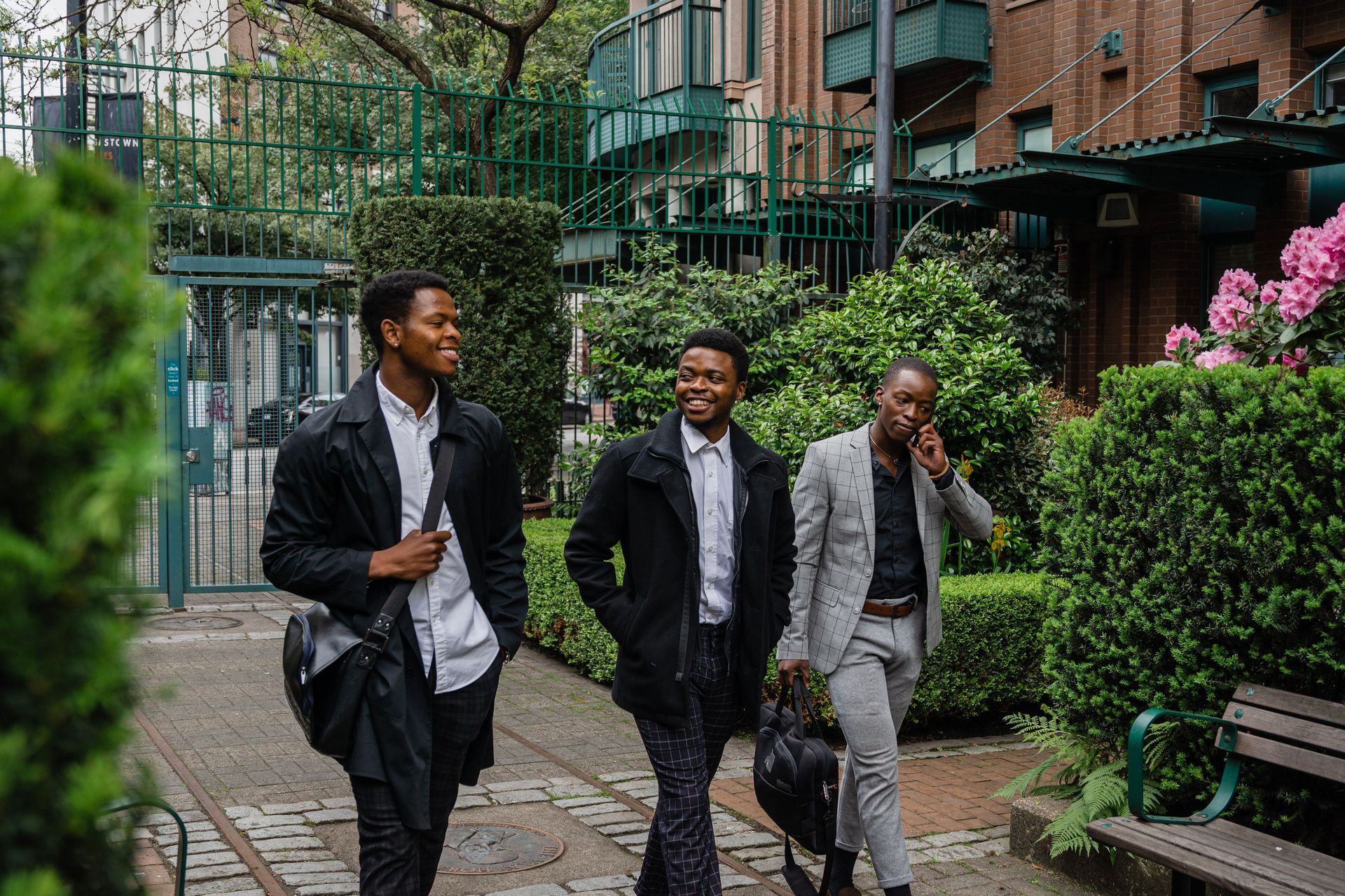 Three men walking and talking in a brick courtyard with greenery and benches.
