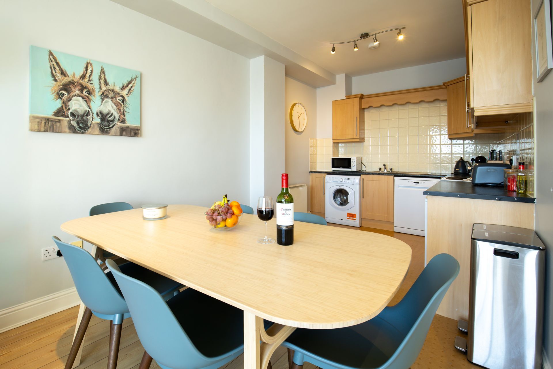 Dining room with oval table, blue chairs, donkey artwork, and a small kitchen.