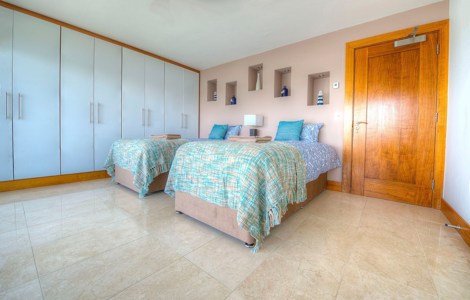 Twin beds in a beige-toned bedroom with blue floral bedspreads and a wooden door.