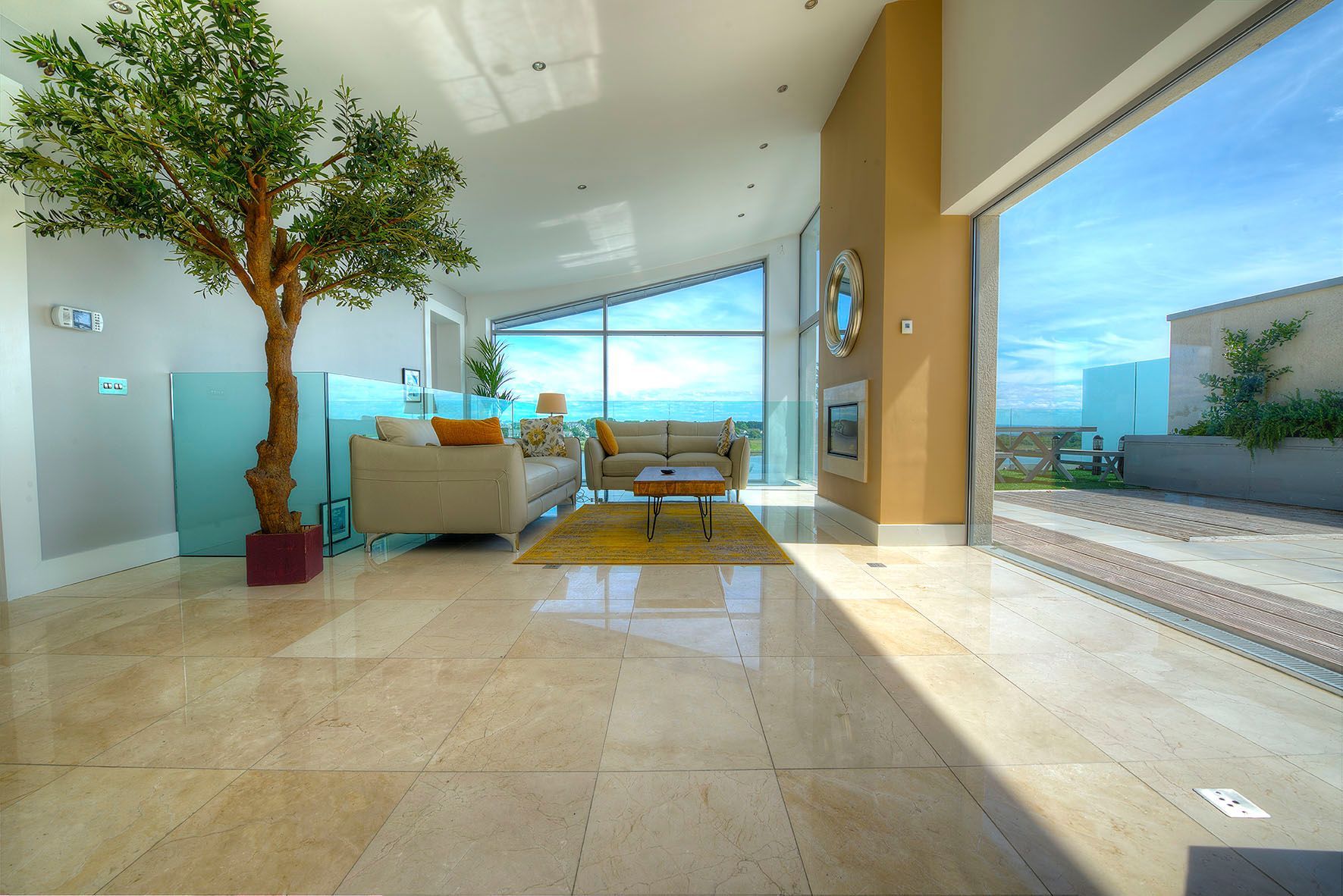 Luxury penthouse living room with lake view, large windows, beige walls, tile floors, and a tree.