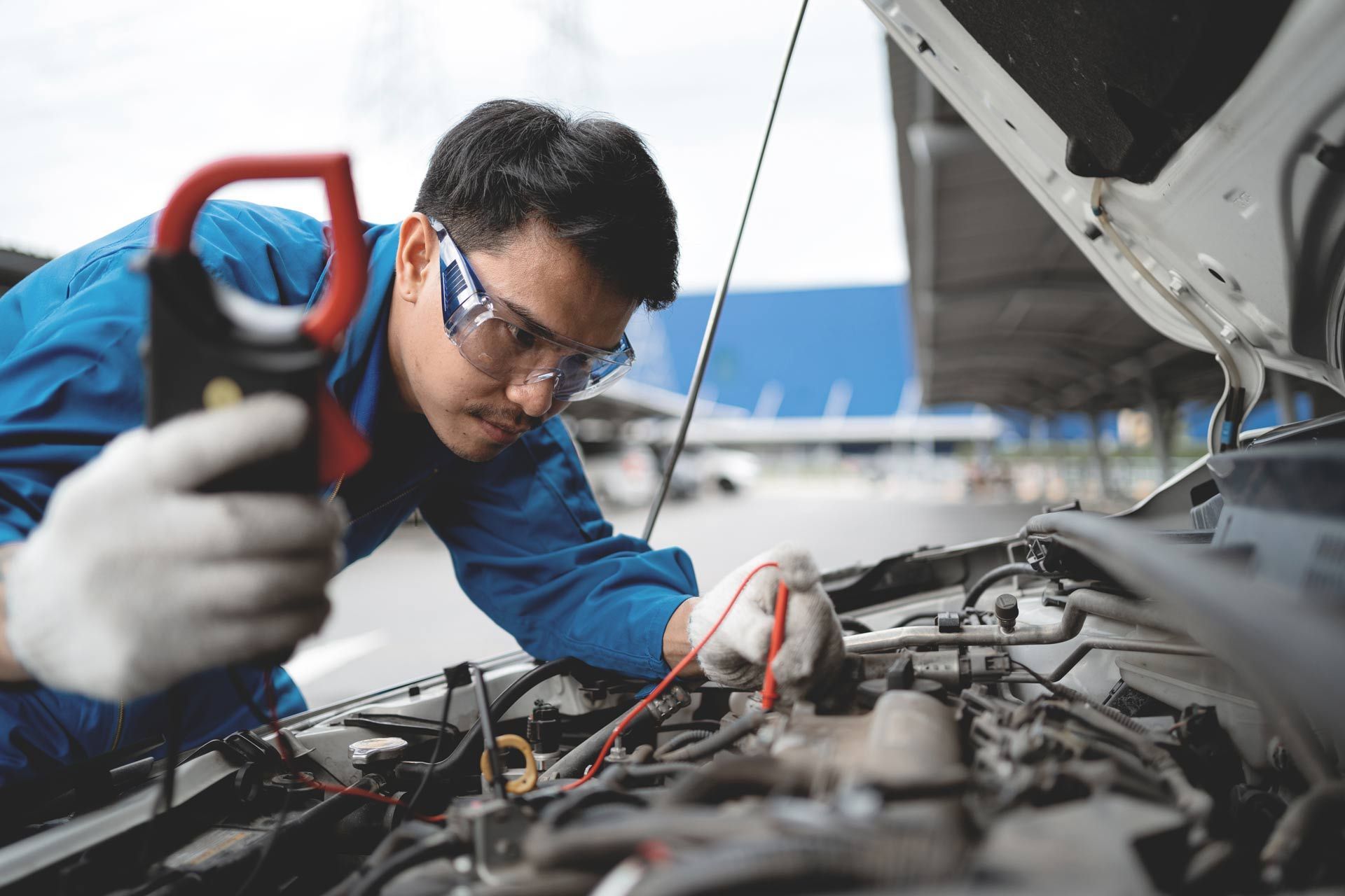 Mechanic inspecting engine with a multimeter under an open car hood