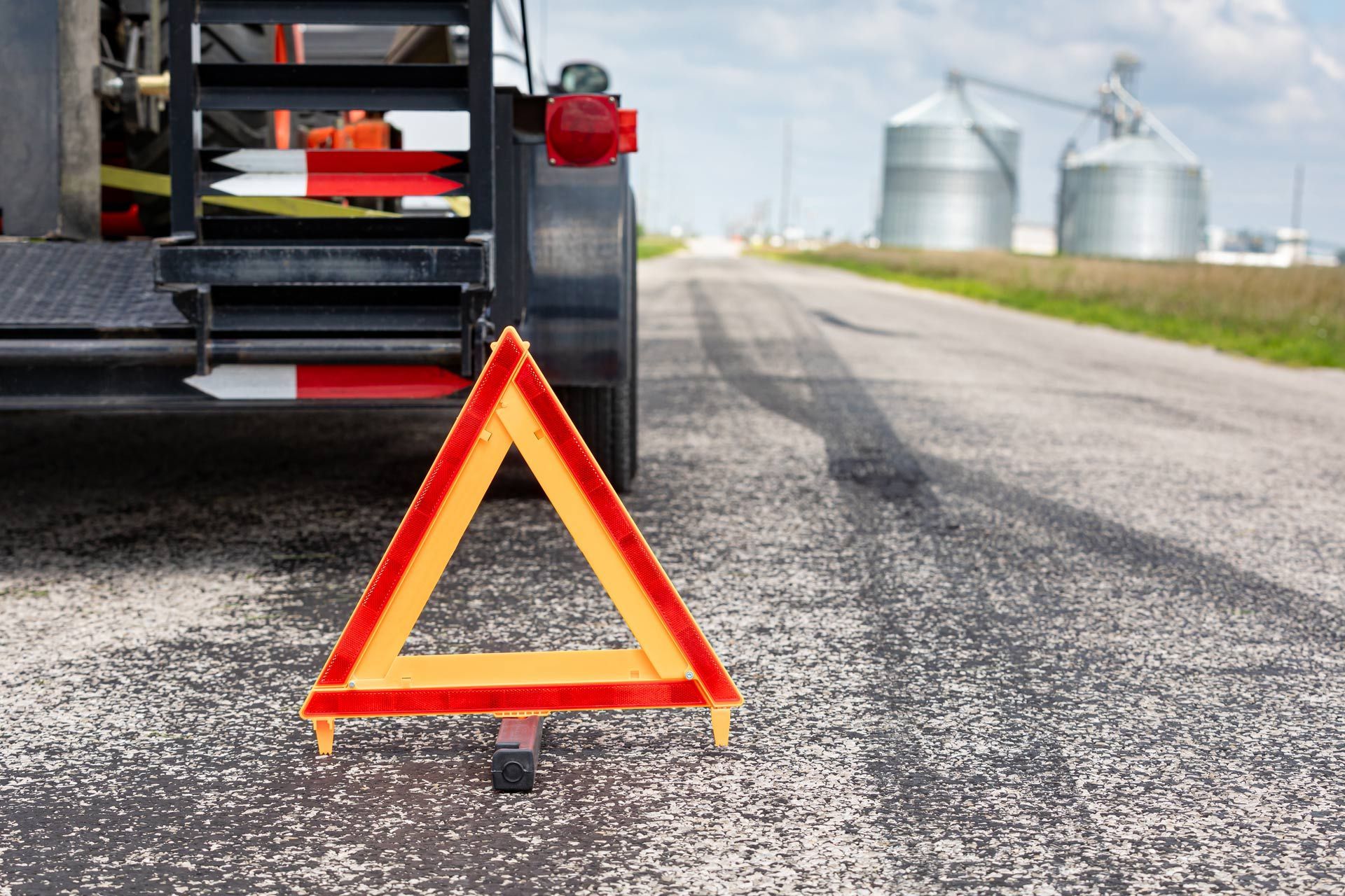 Red warning triangle behind a truck on a roadside near grain silos
