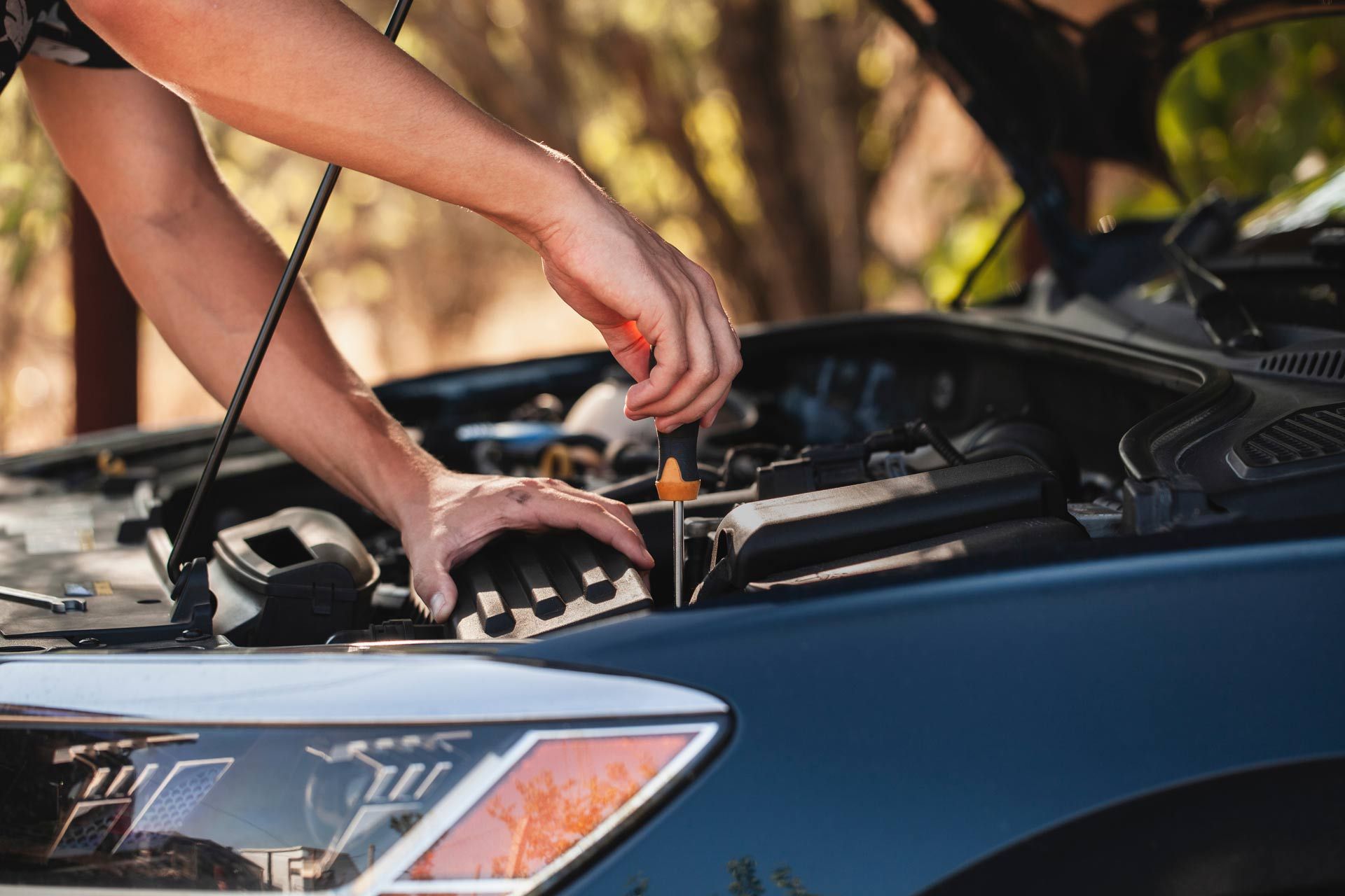 Person charging a black car battery with jumper cables under the open hood