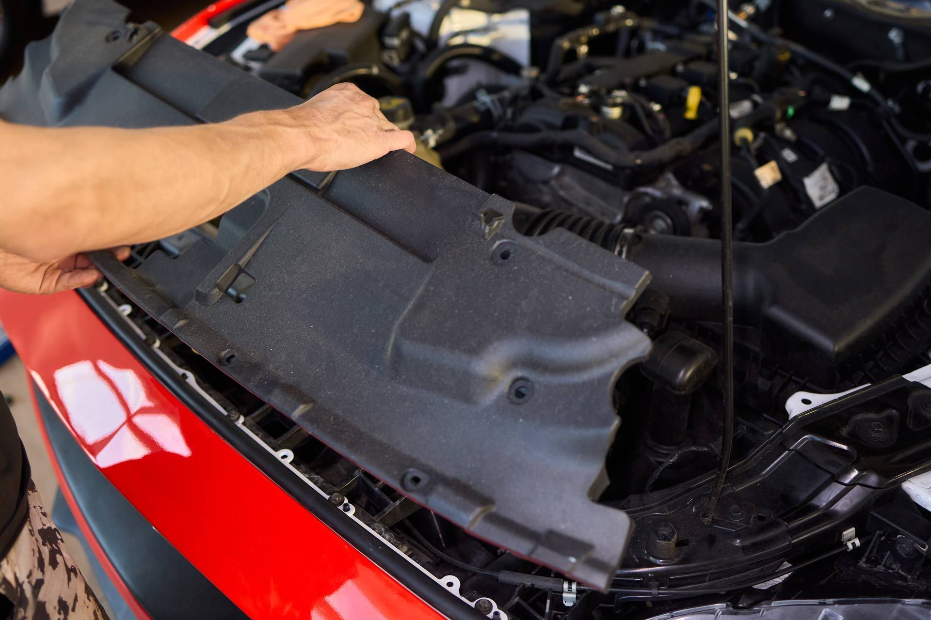 Person lifting a black car engine cover in a red vehicle’s open hood