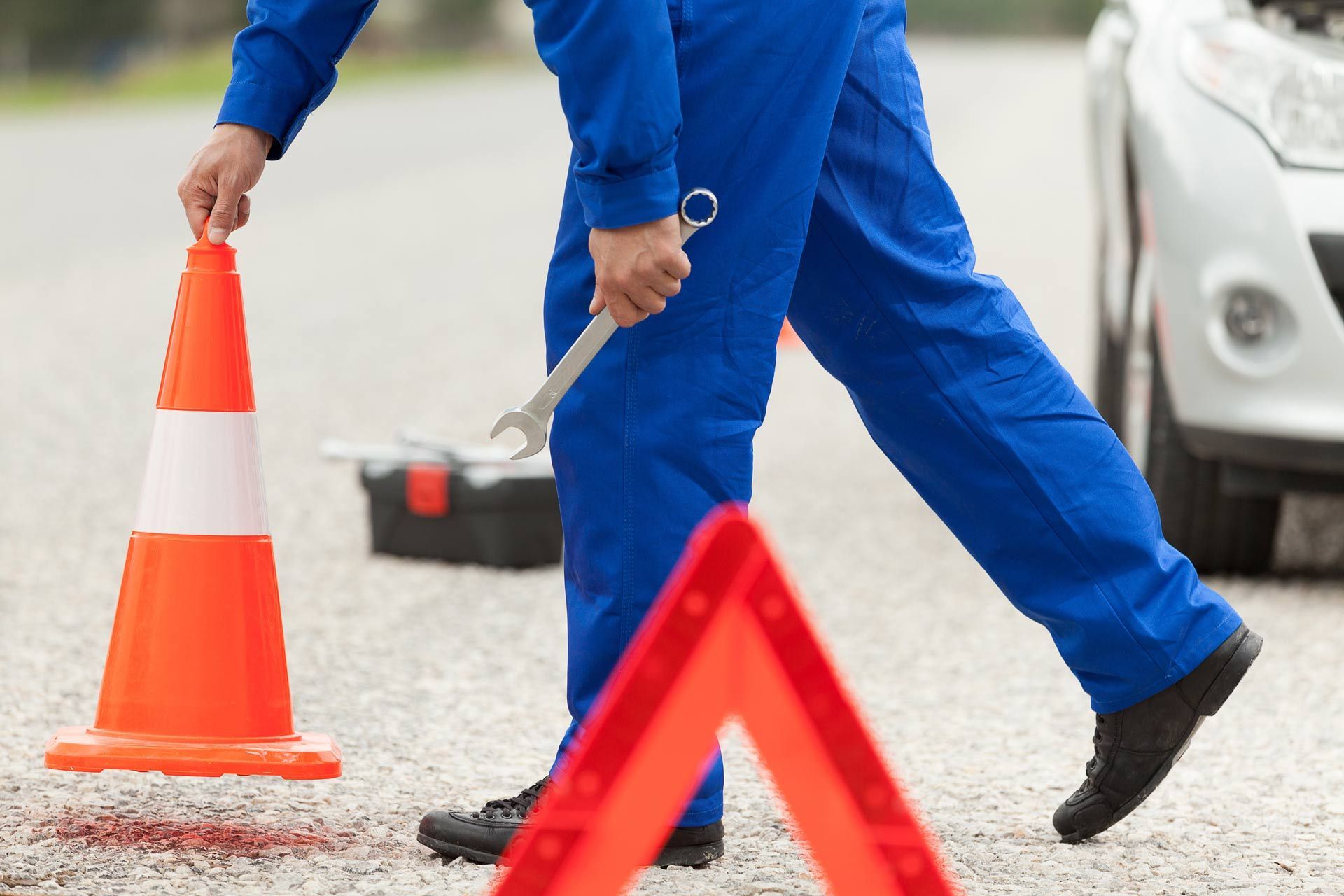 Workers placing orange traffic cones on a road near a car, marking a work zone