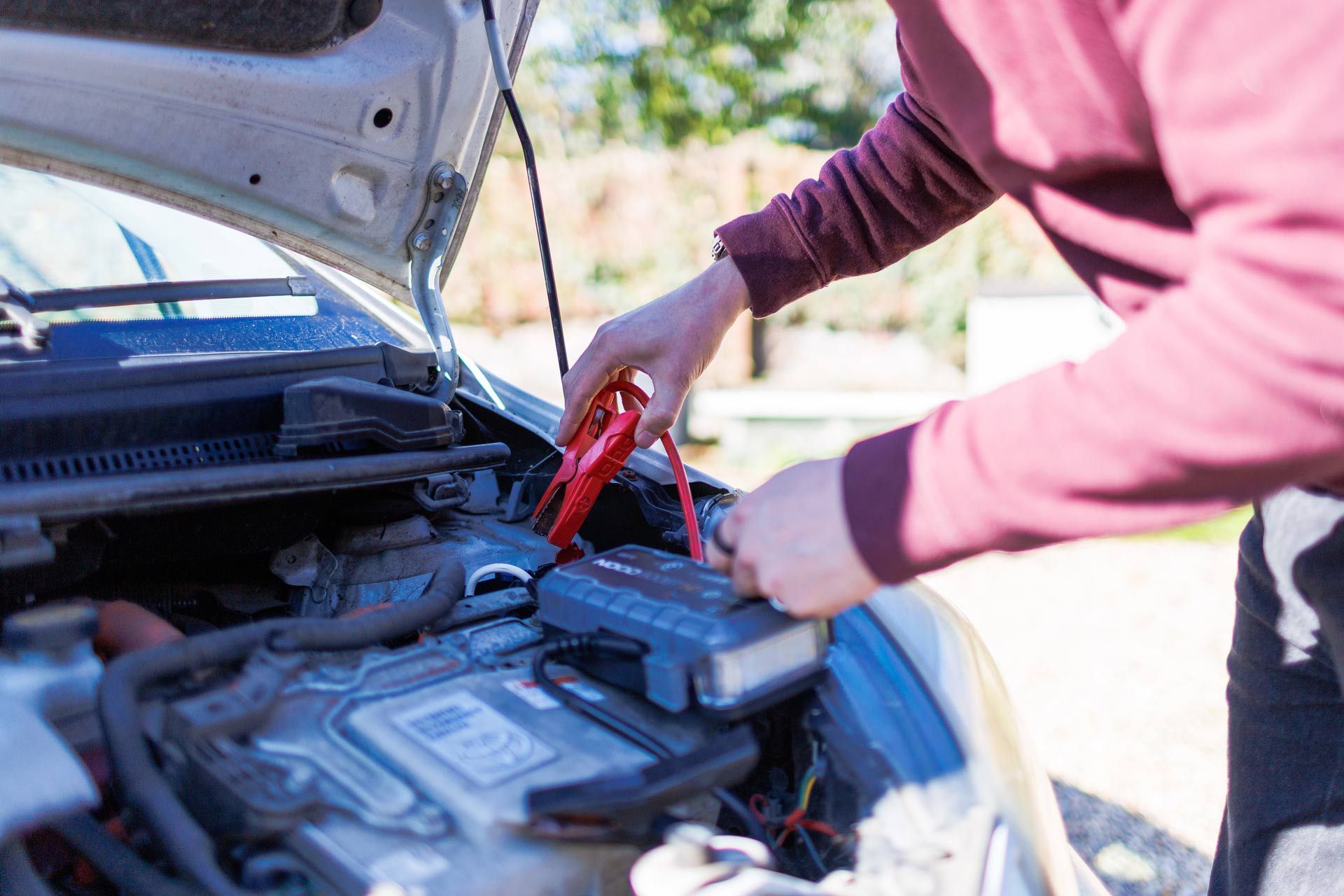 Person using jumper cables to start a car with the hood open