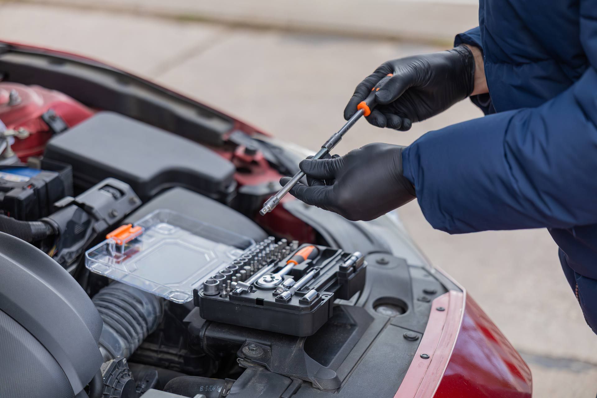 Gloved hands using a screwdriver to repair a car battery in an open engine bay