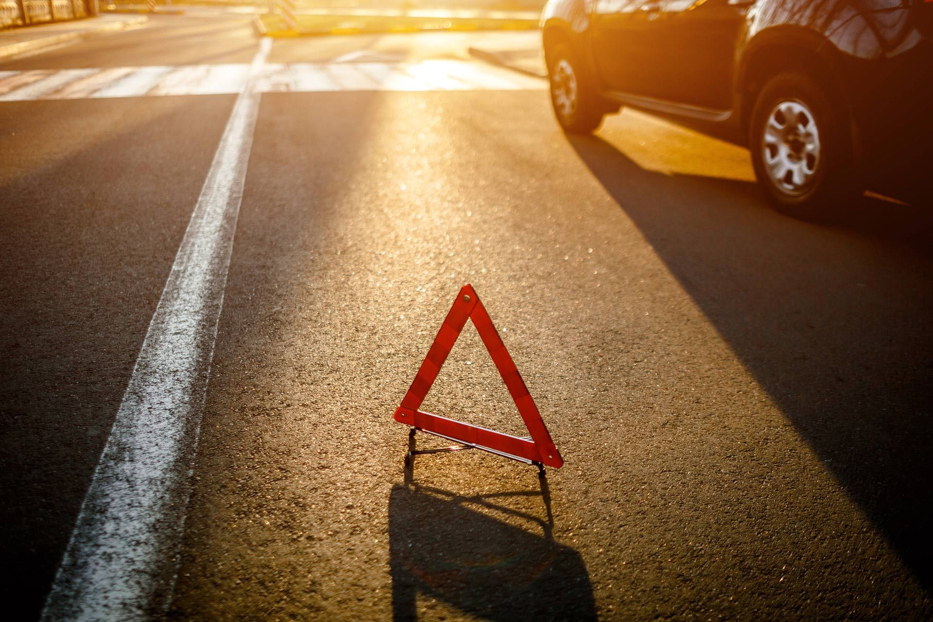 Red warning triangle on sunlit road beside a car, suggesting a breakdown.