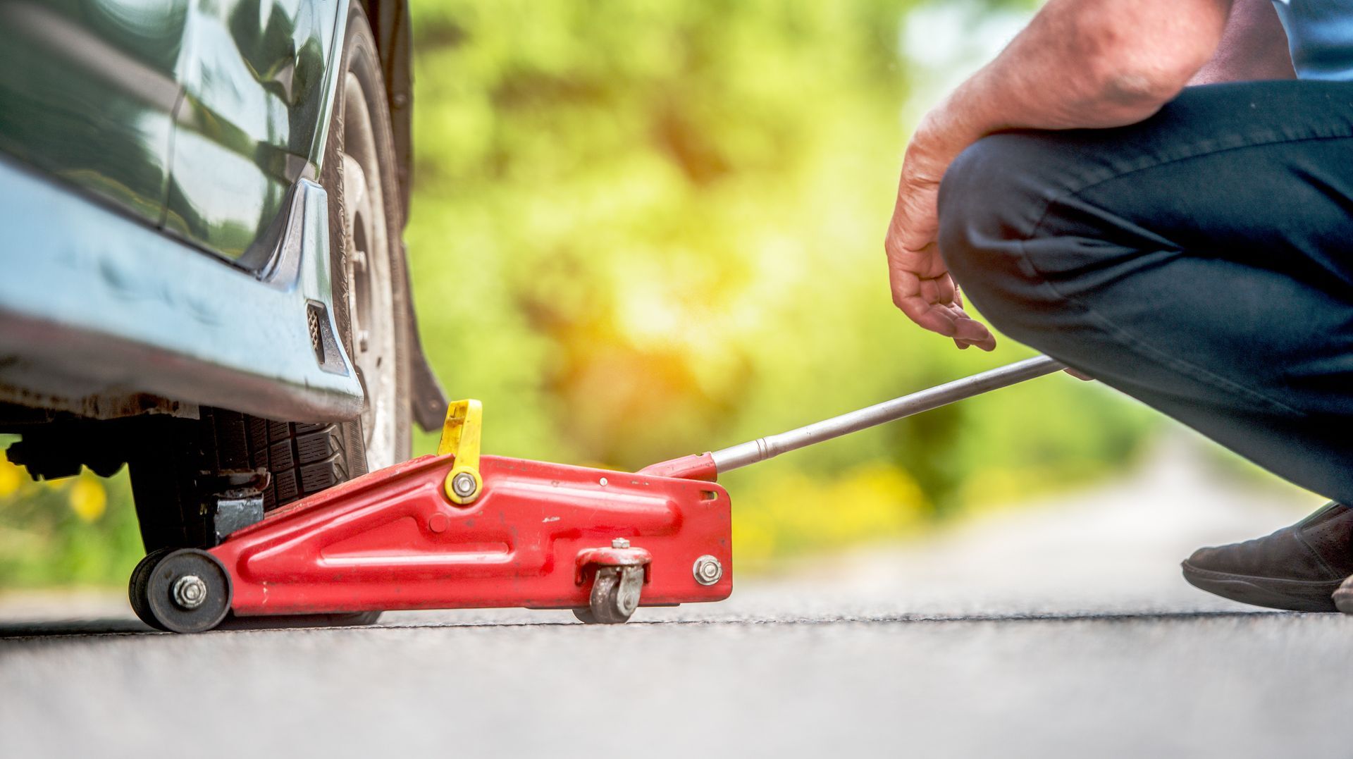 Person using a red floor jack to lift a car tire on a driveway
