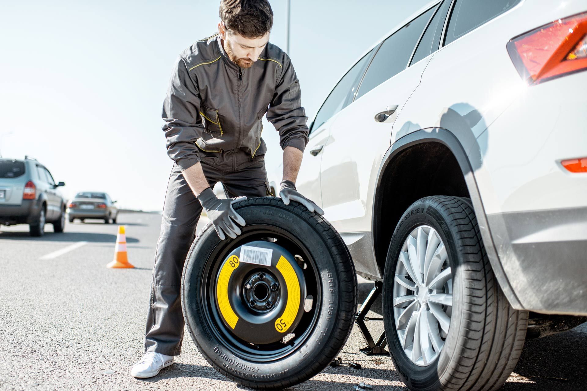 Man changing a car tire beside a white SUV on a roadside