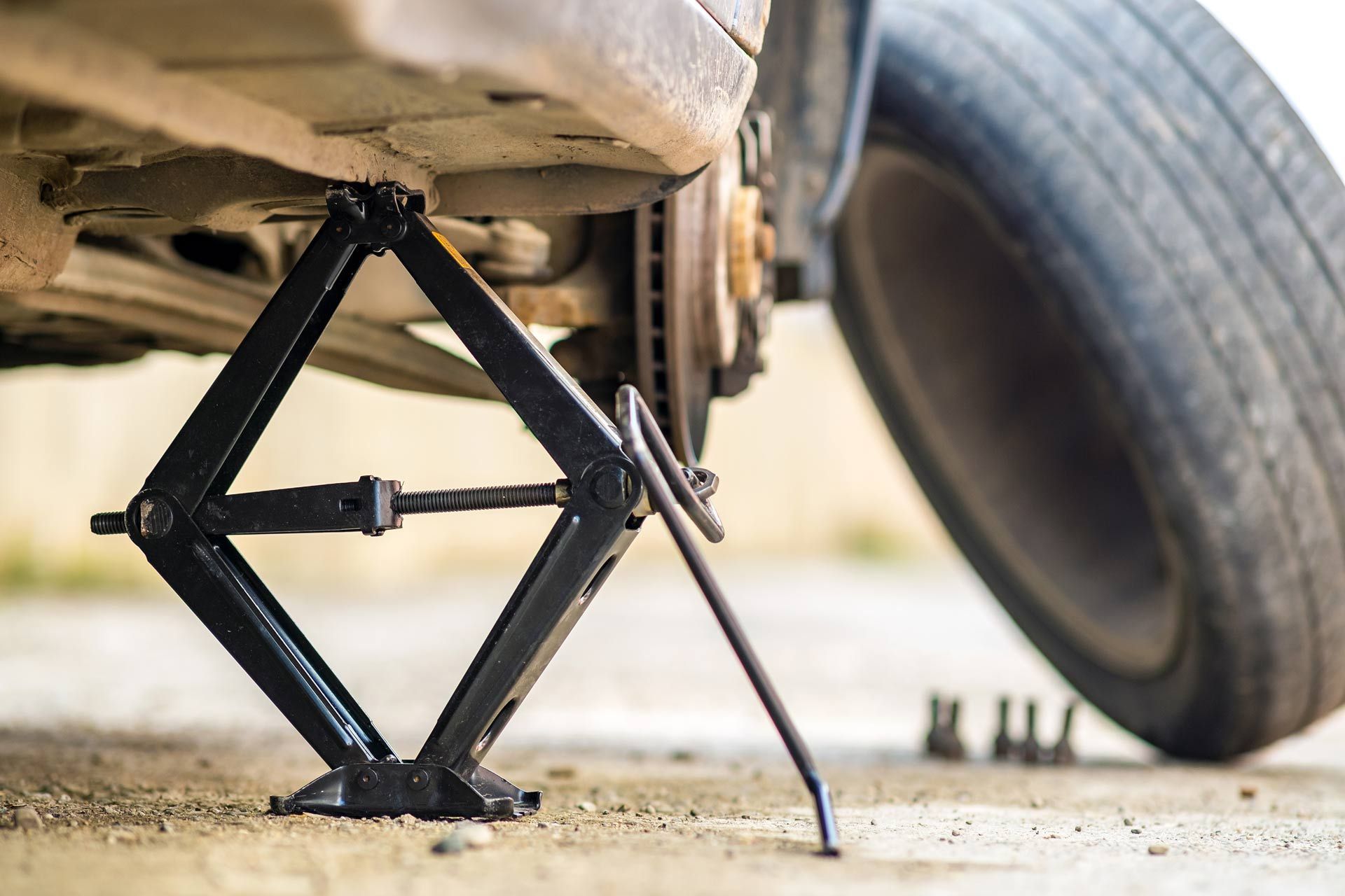 Car jack lifting a vehicle to change a tire, with a spare tire nearby on pavement