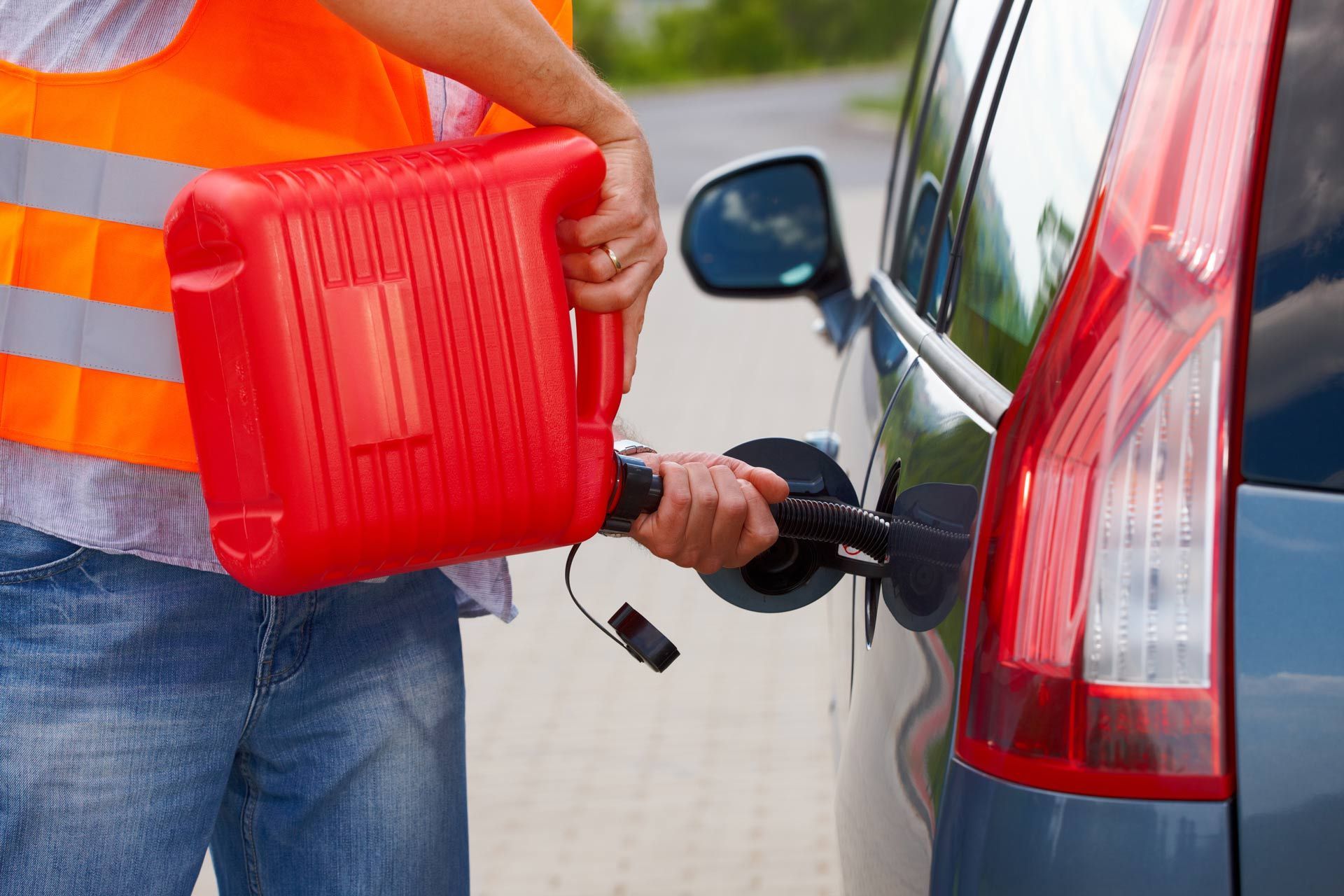 Person in orange vest refueling a car with a red gas can