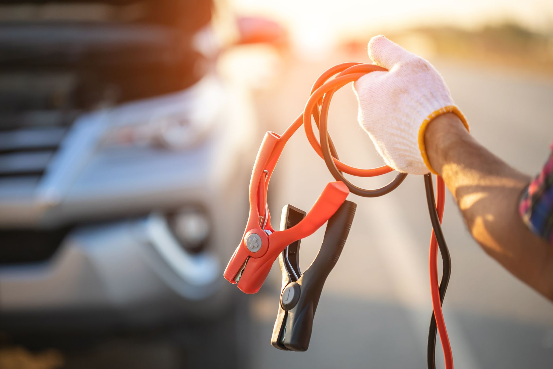 Hand holding red jumper cables beside a car in bright sunlight