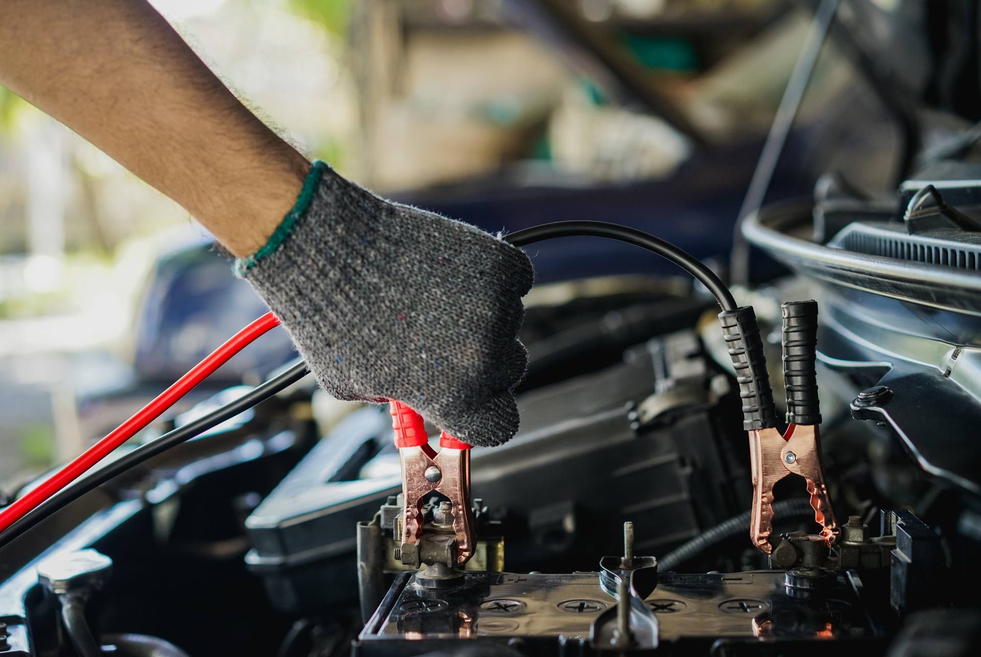 Gloved hands using jumper cables to jump-start a car battery under the hood