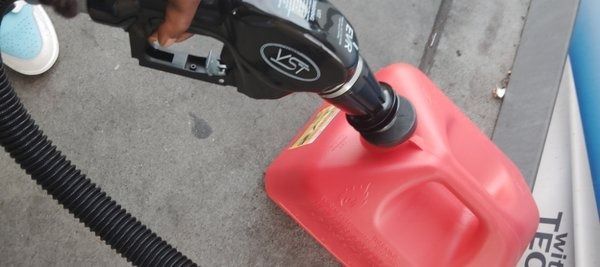 Gas pump nozzle filling a red plastic fuel can outdoors.