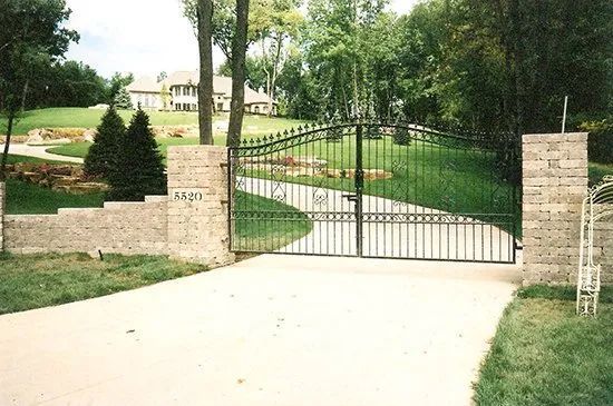 A driveway with a gate and a brick wall leading to a house.