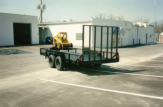 A trailer with a yellow forklift on it is parked in a parking lot.