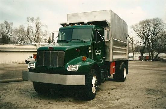 A green dump truck is parked in a parking lot