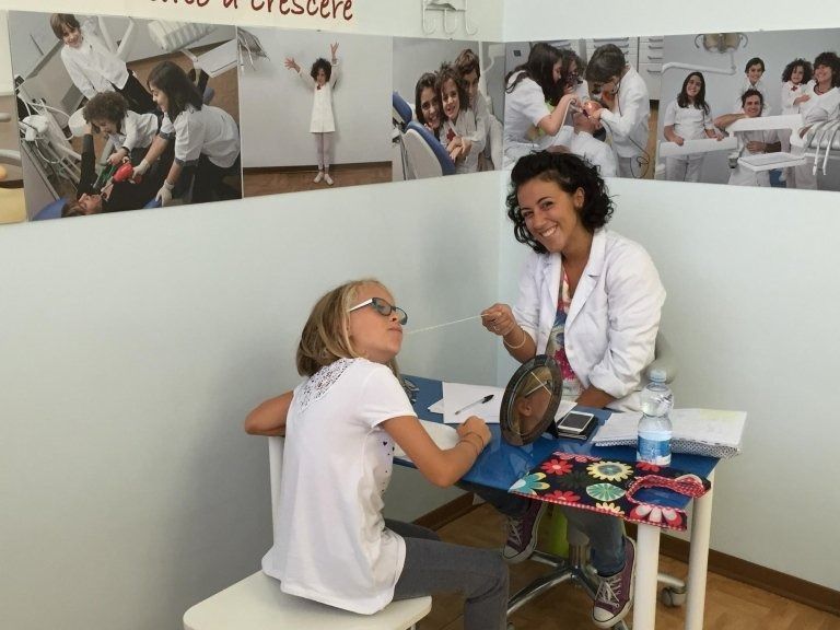 Due donne che conversano a un tavolino in una clinica o in un ufficio luminoso, con poster sulla salute alle pareti.