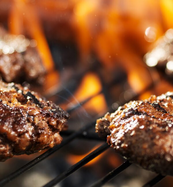 Hamburgers are cooking on a grill with flames in the background