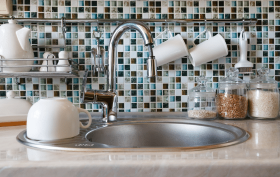 A kitchen sink with a mosaic tile wall and a faucet.