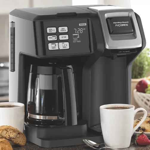 A coffee maker is sitting on a counter next to cups of coffee and cookies.