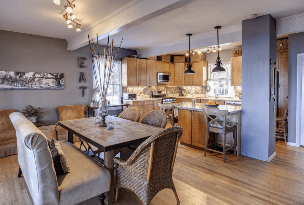 A dining room with a table and chairs and a kitchen in the background.
