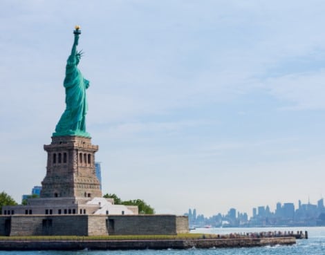The statue of liberty is sitting on top of a small island in the middle of the ocean.