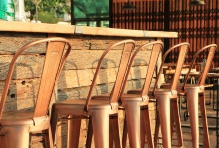 A row of copper bar stools are lined up in front of a wooden bar.