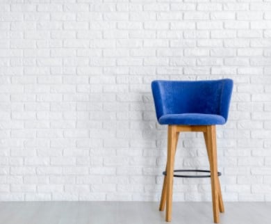 A blue bar stool is sitting in front of a white brick wall.