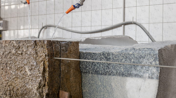 A hose is spraying water on a stone wall.
