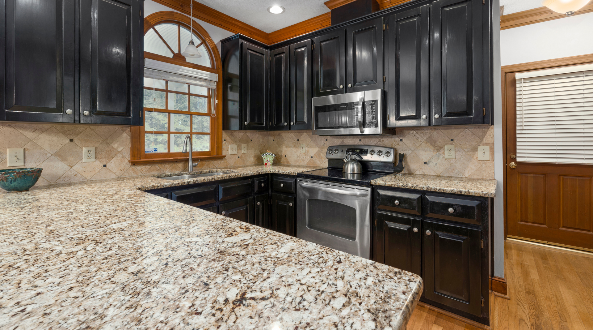 A kitchen with granite counter tops , black cabinets and stainless steel appliances.