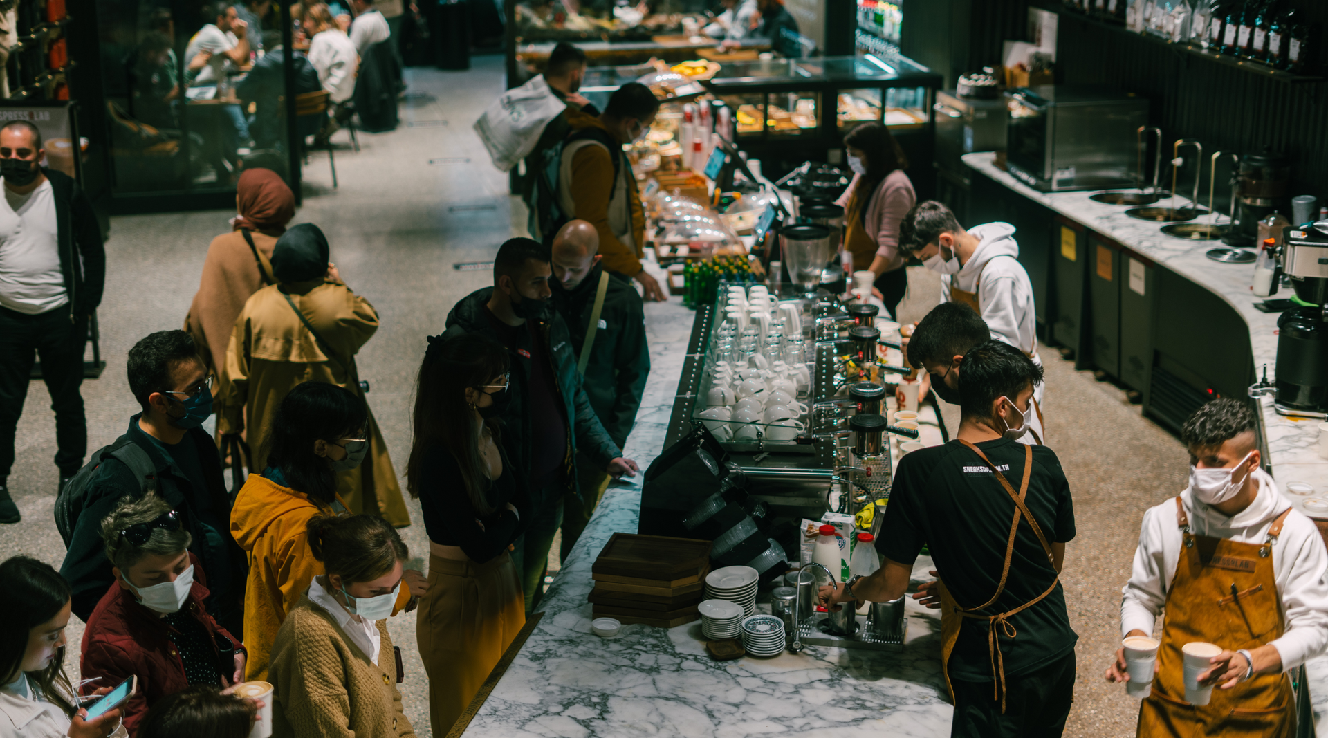 A group of people wearing face masks are standing around a counter in a restaurant.