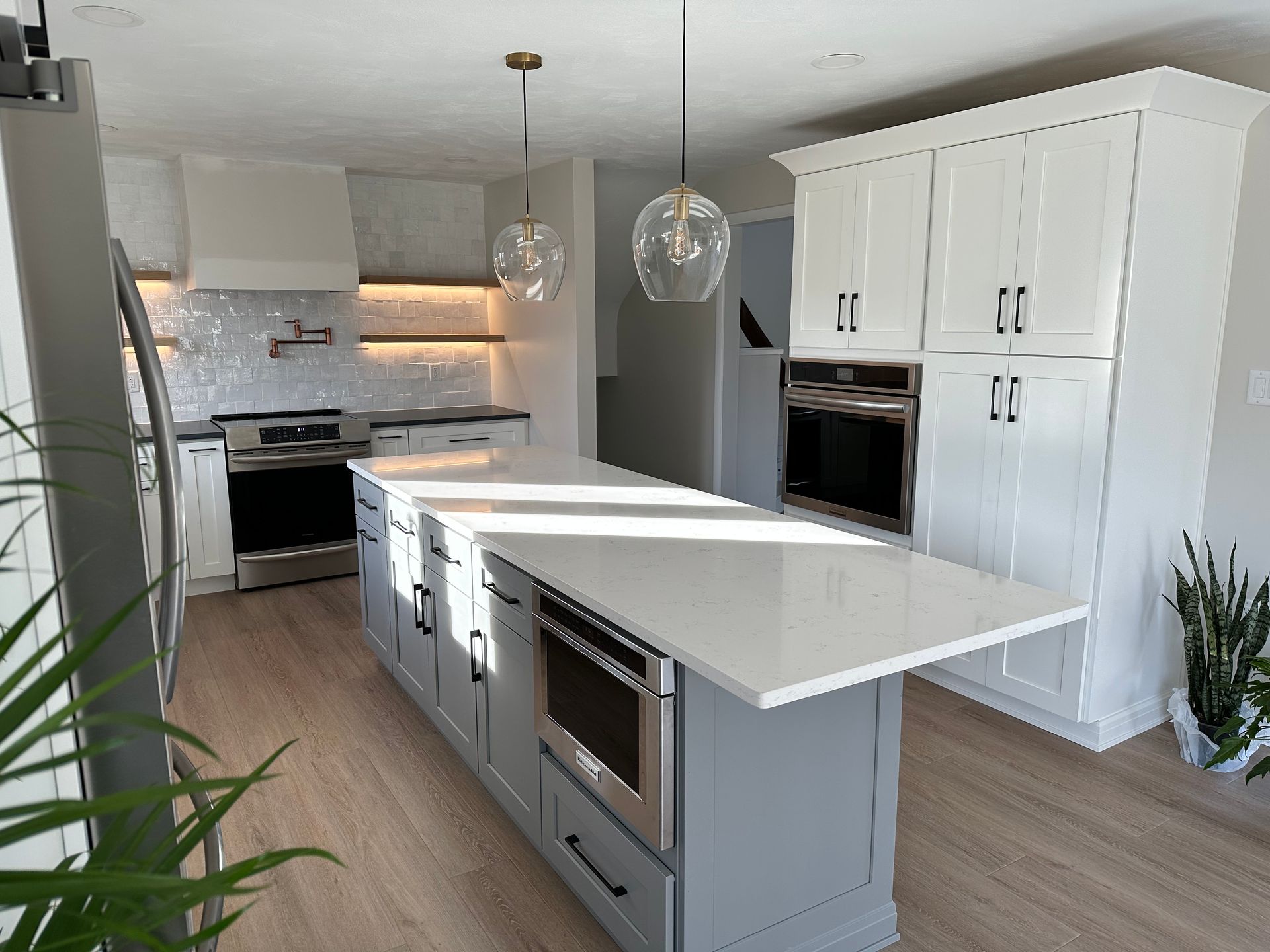 Modern kitchen with gray island, white cabinets, and stainless steel appliances.