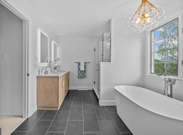 Modern bathroom with a bathtub, shower, vanity, and window. Gray floor, white walls, and a decorative light.