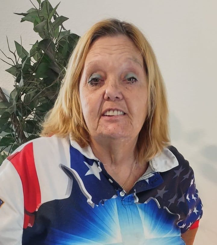 Woman in a patriotic star-spangled shirt standing indoors beside a potted plant