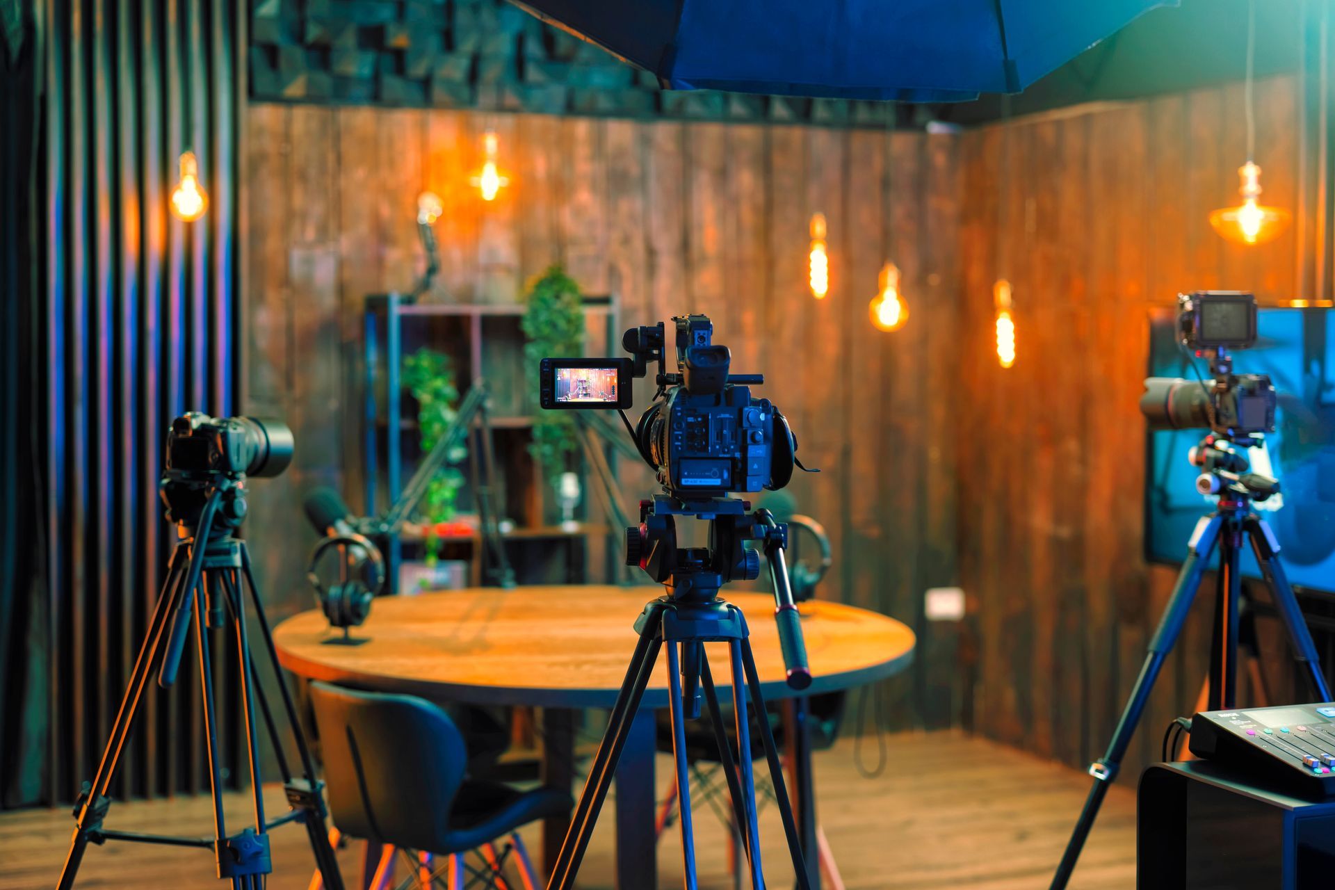 Camera crew in a studio with tripods, lights, and a round table against a wooden backdrop.