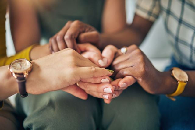 Several hands stacked together in a teamwork gesture, with wristwatches visible.