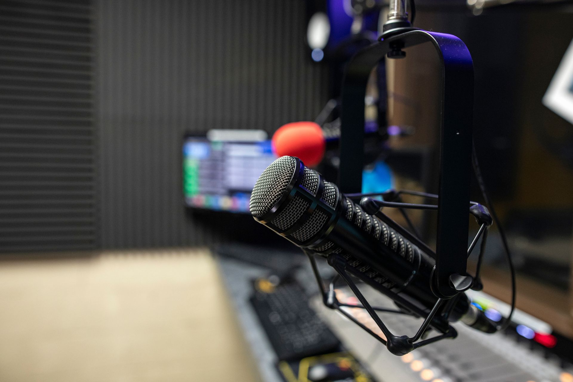 Close-up of a studio microphone on a boom arm in a recording booth, with a blurred mixing console in the background