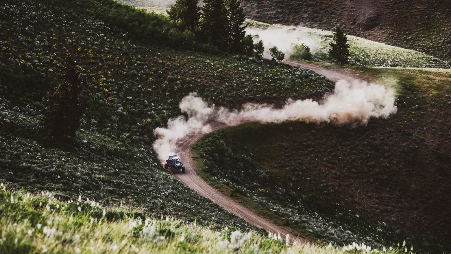 A car is driving down a dirt road in the mountains. hay flats. meeker colorado