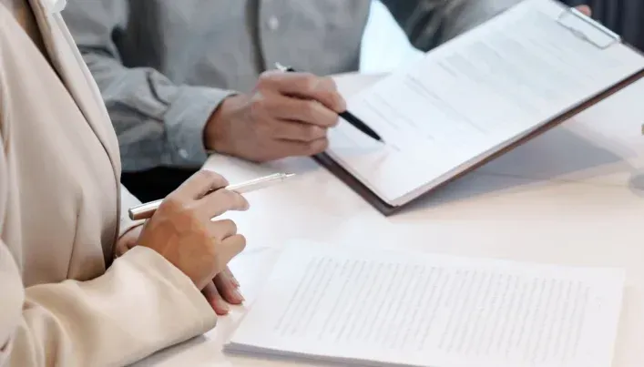 Two people sit at a table reviewing and signing business documents.
