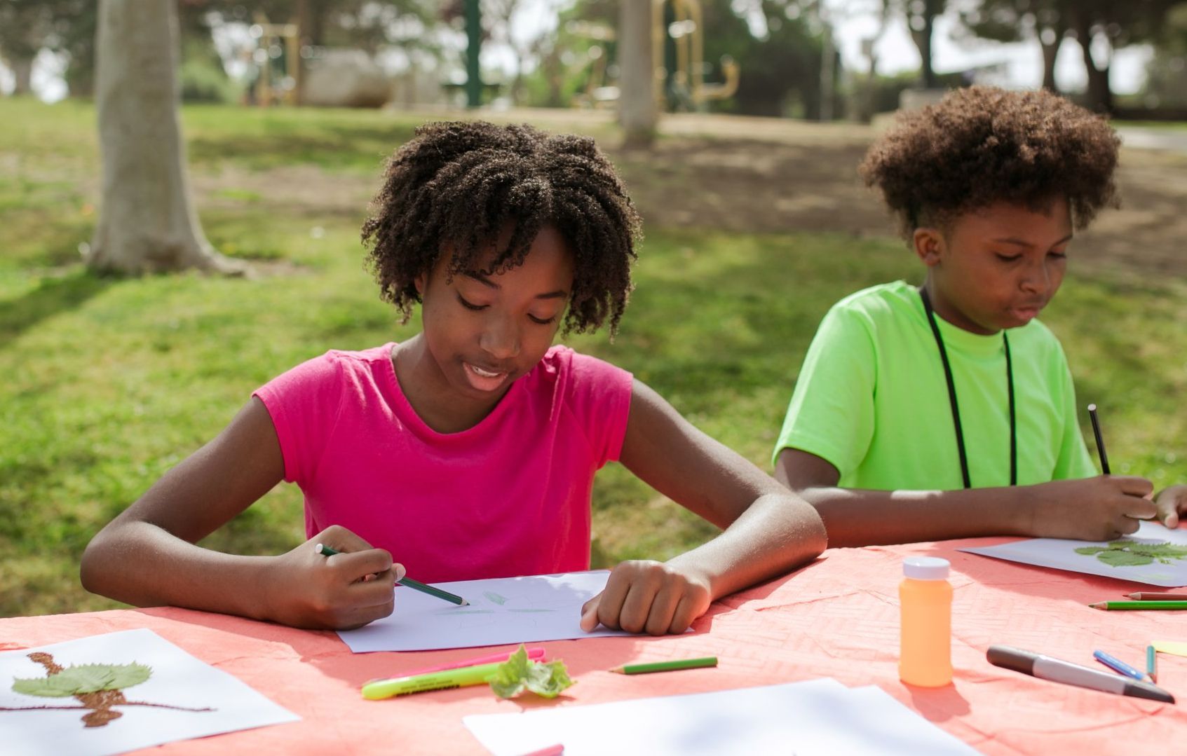 Children enjoying an outdoor art activity, drawing with colored pencils on a picnic table.