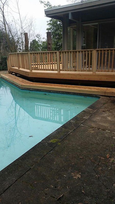 Wooden deck surrounds a pool. The water reflects the deck and trees.