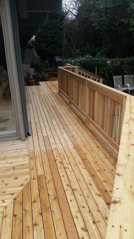 Wooden deck with ramp and railing, leading to a yard with trees.