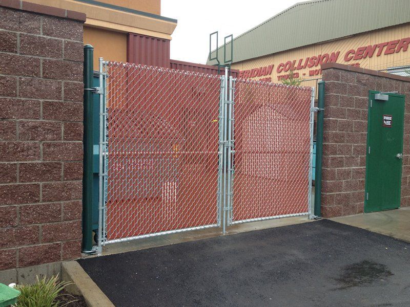 Red-covered chain-link gates between brick walls; opens to parking lot, building in background.