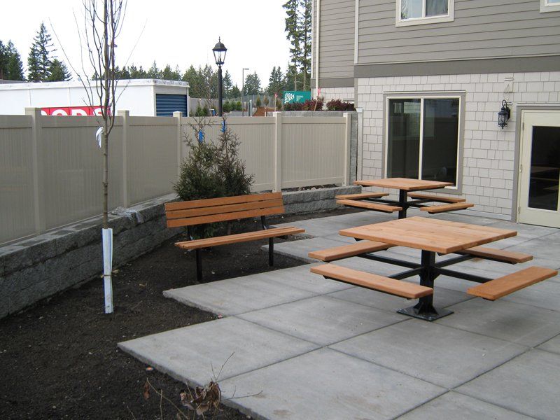 Outdoor patio with concrete pavers, picnic tables, bench, and beige fence.
